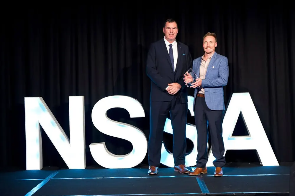 Two of the Guardian team holding an NSSA award in front of the NSSA letters