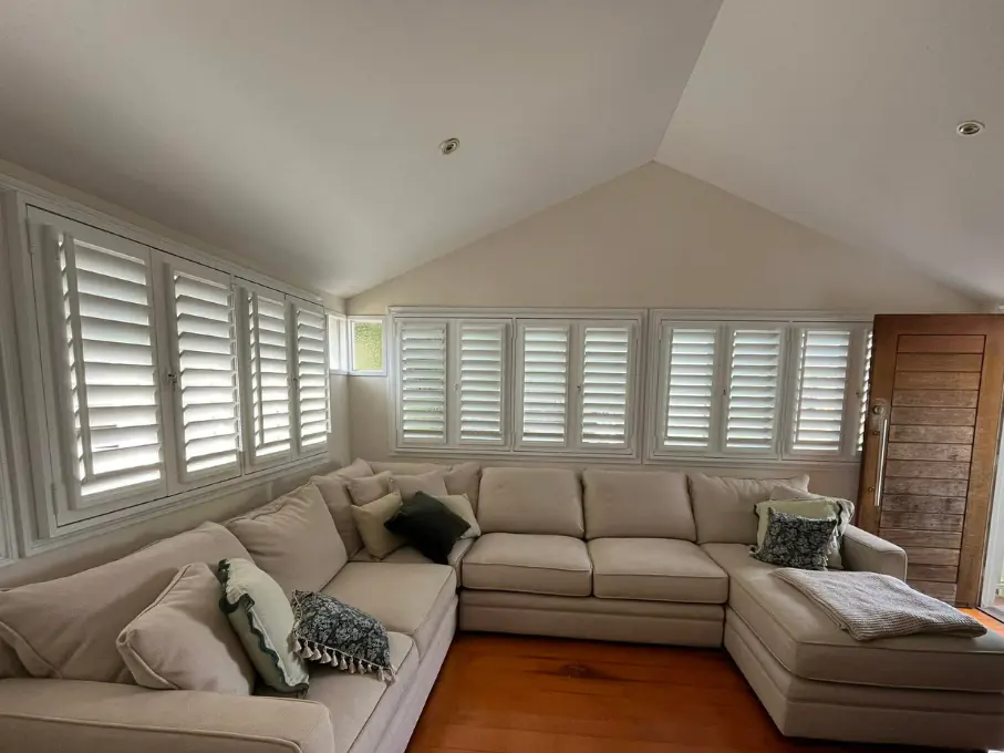 The same lounge room after Guardian, white aluminium shutters across every window, blades tilted open to the light