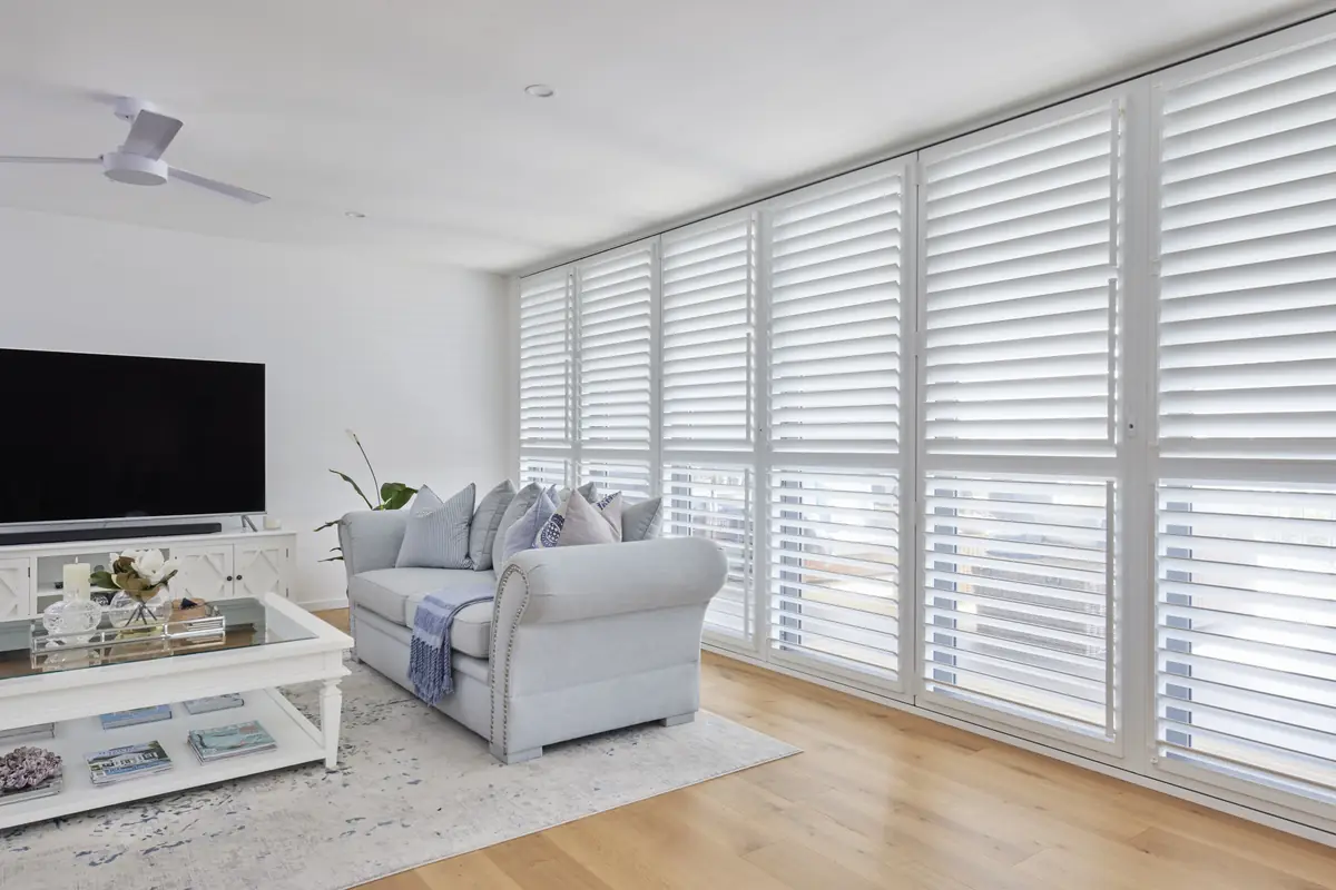 A bright living room with Guardian aluminium shutters closed across a full wall of windows