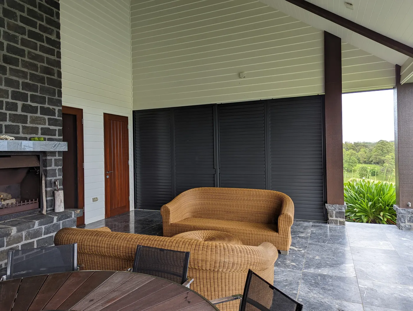 A covered Brisbane patio closed in with dark four-panel Guardian sliding shutters, cane lounges in front