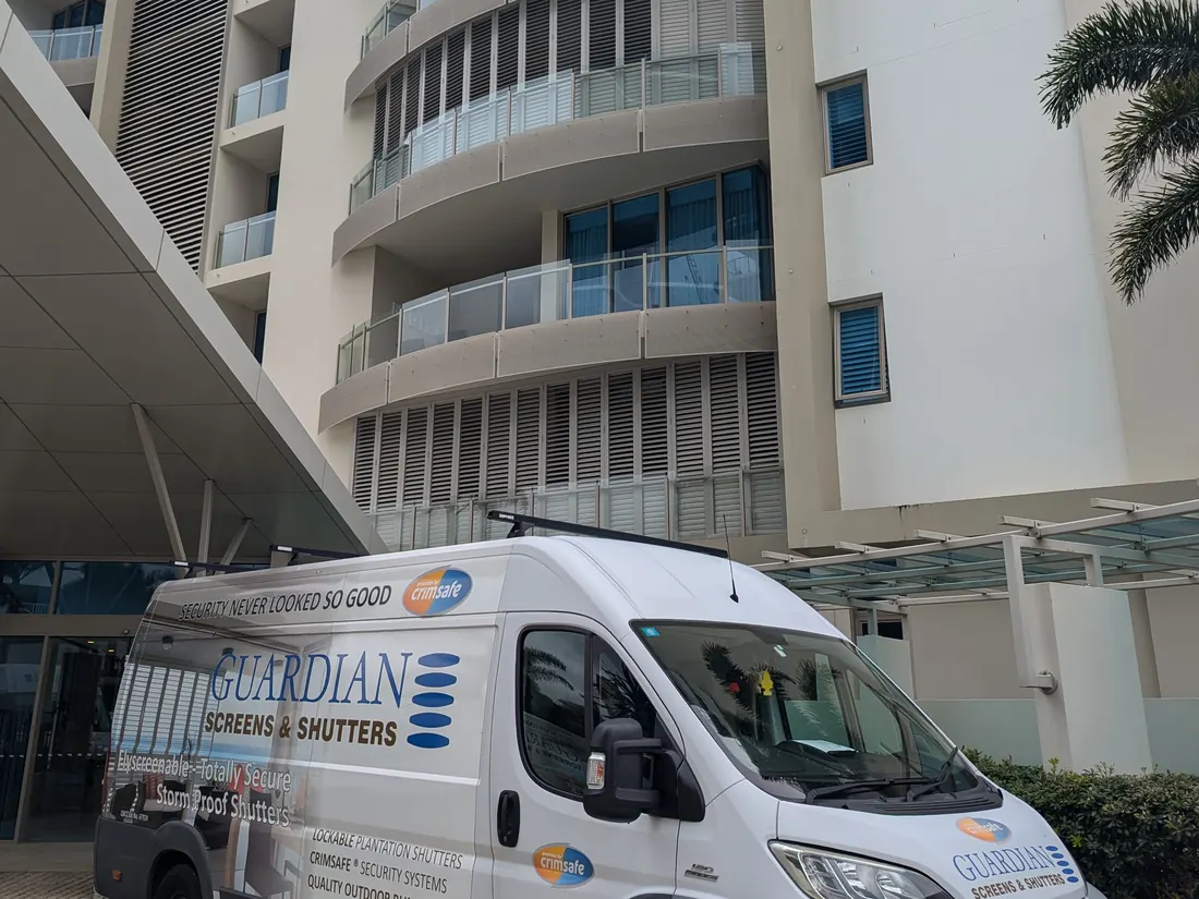 A Guardian Screens & Shutters van parked outside an apartment tower with aluminium shutters on its balconies